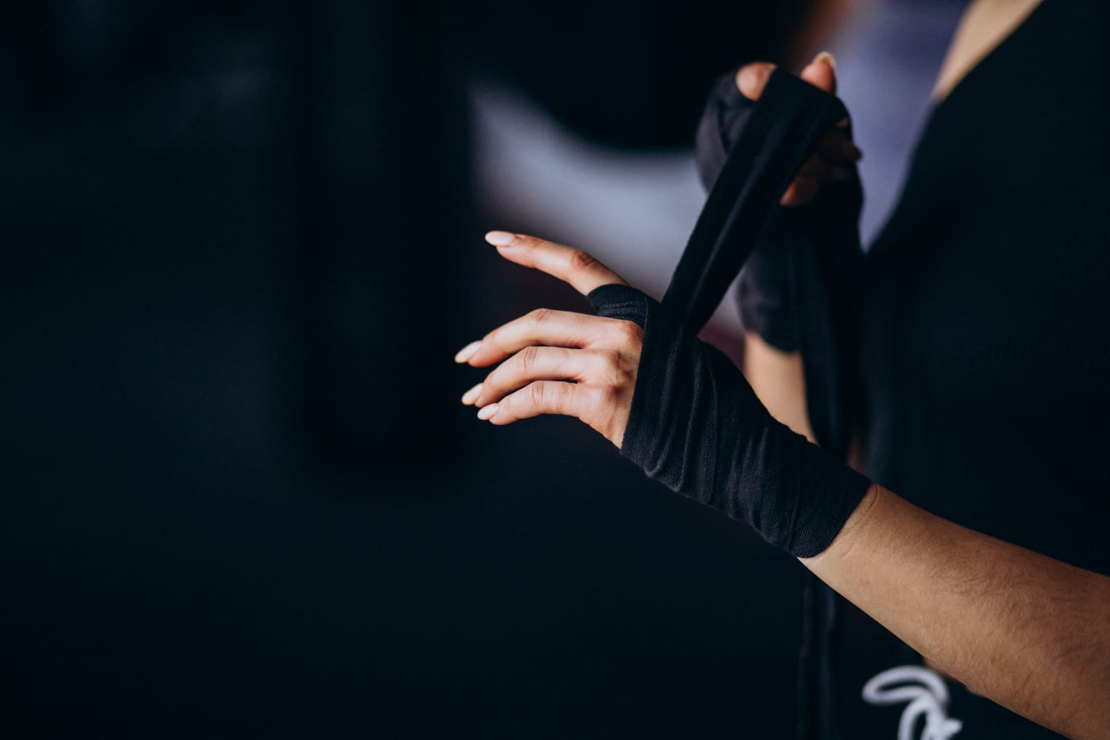 Close-up of a trainer wrapping a black hand wrap around a woman's hand.